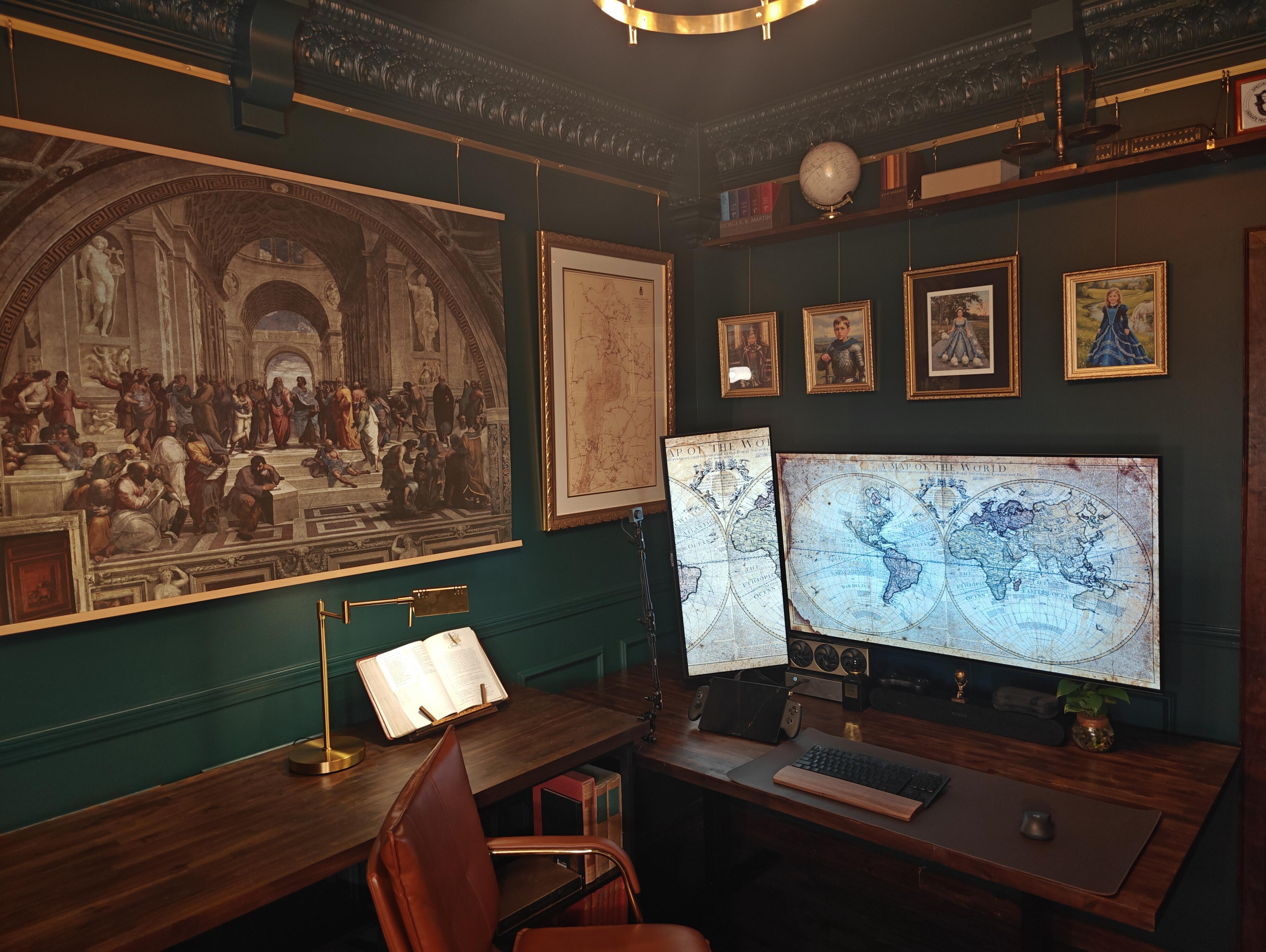 A study with dark green walls, a pressed plaster cornice and gilt-framed portraits. A wide screen and a second screen stood on its end both show an antique map of the world, over a dark wood desk with a handheld PC and a keyboard.